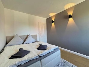 A bedroom with a bed, pillows, a door, and wall-mounted lighting. - Bayfront Escape - Stylish time out by the water in Travemünde (Lübeck)