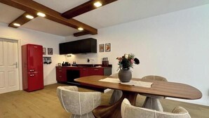 Eine moderne Küche mit Einbauofen, einem roten Kühlschrank und einem Essbereich mit Holztisch und zwei Stühlen.
