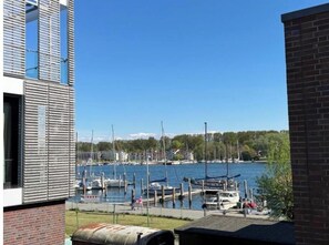 A marina with boats docked, a clear sky, and a forested hill in the background. - Bayfront Escape - Stylish time out by the water in Travemünde (Lübeck)