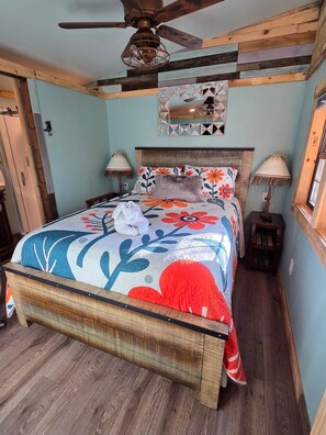 A bedroom with a wooden bed, two bedside lamps, a ceiling fan, and a decorative mirror above the bed.