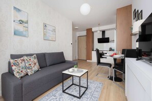 Una sala moderna con un sofá gris, una mesita auxiliar y un comedor con una mesa blanca y sillas negras.