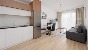 A modern kitchen with a built-in refrigerator, a dining area with a table and chairs, and a grey sofa in a living area. - Comfortable Apartment | Parking (Warszawa)