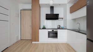 A modern kitchen with white cabinets, a black range hood, and a stainless steel refrigerator. - Comfortable Apartment | Parking (Warszawa)