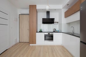 A modern kitchen with white cabinets, a black range hood, and a stainless steel refrigerator. - Comfortable Apartment | Parking (Warszawa)