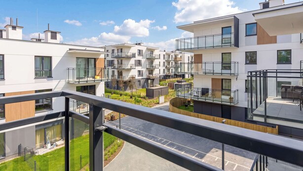 A modern apartment complex with multiple balconies, a rooftop garden, and a clear view of the sky. - Comfortable Apartment | Parking (Warszawa)