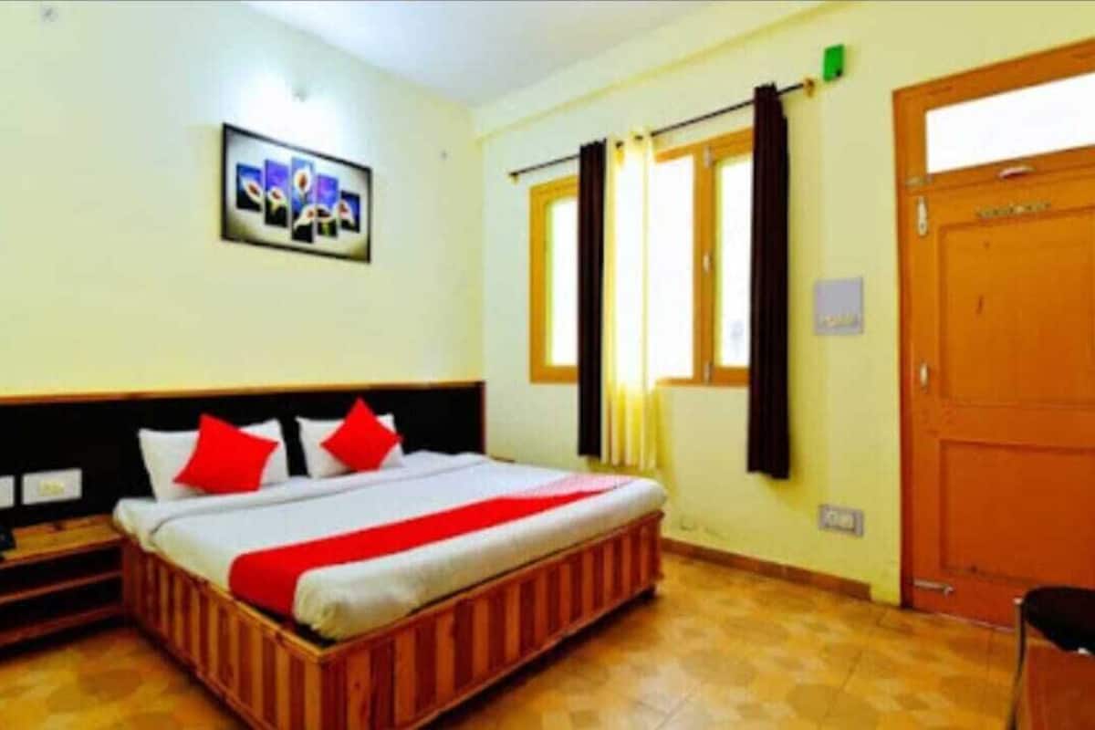 A hotel room with a bed, a nightstand, a window with curtains, and a door.