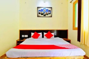 A single bed with a red and white bedspread, a headboard, and a nightstand with a lamp. - Chaman Vatika (Kasol)