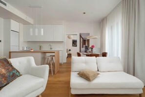 Ein modernes Wohnzimmer mit einer Couch, einem Essbereich mit Tisch und Stühlen sowie einer Küche mit Schränken und einer Arbeitsplatte.