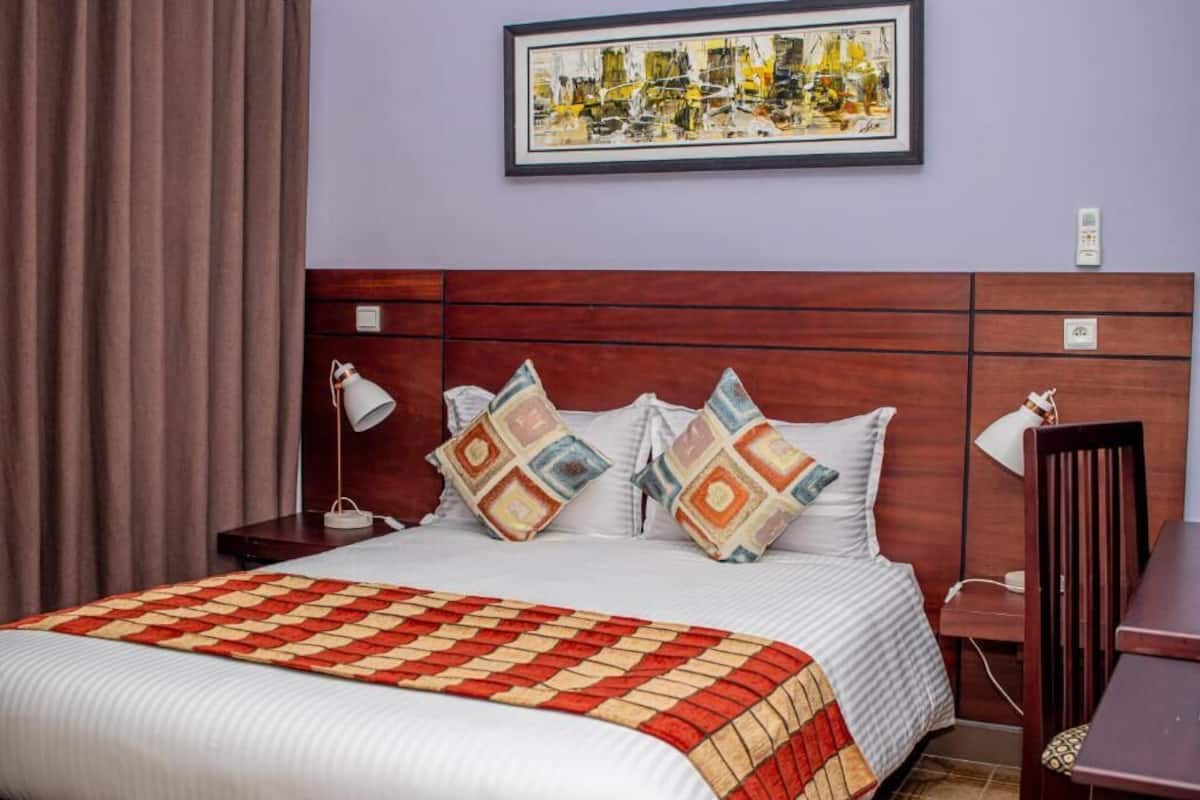 Una habitación de hotel con una cama grande, cabecero de madera, una obra de arte enmarcada en la pared y un escritorio con una silla.