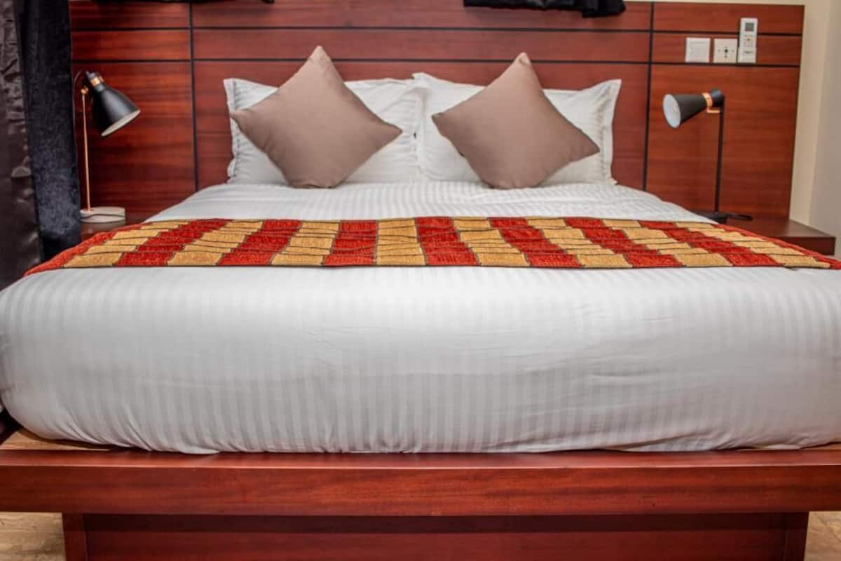 Una cama bien hecha con un edredón estampado, dos almohadas y una lámpara de noche.