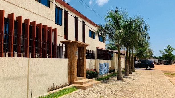 A building with a paved driveway, a gated entrance, and a parked car. - résidence hoteliere lauria (Lomé)