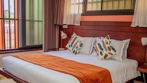 A hotel room with a large bed, a window with curtains, a bedside lamp, and a patterned throw blanket. - résidence hoteliere lauria (Lomé)