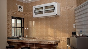 A kitchen with a tiled backsplash, a built-in microwave, a refrigerator, and a window with bars. - résidence hoteliere lauria (Lomé)