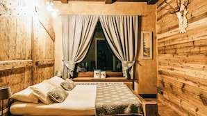 Een rustieke houten kamer met een bed, houten wanden, een raam met gordijnen en een opgehangen dierenkop aan de muur.