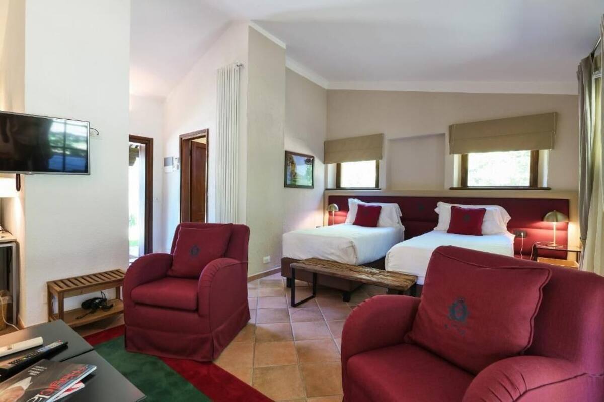 Quarto de hotel com duas camas, televisão, escrivaninha e cadeiras vermelhas.