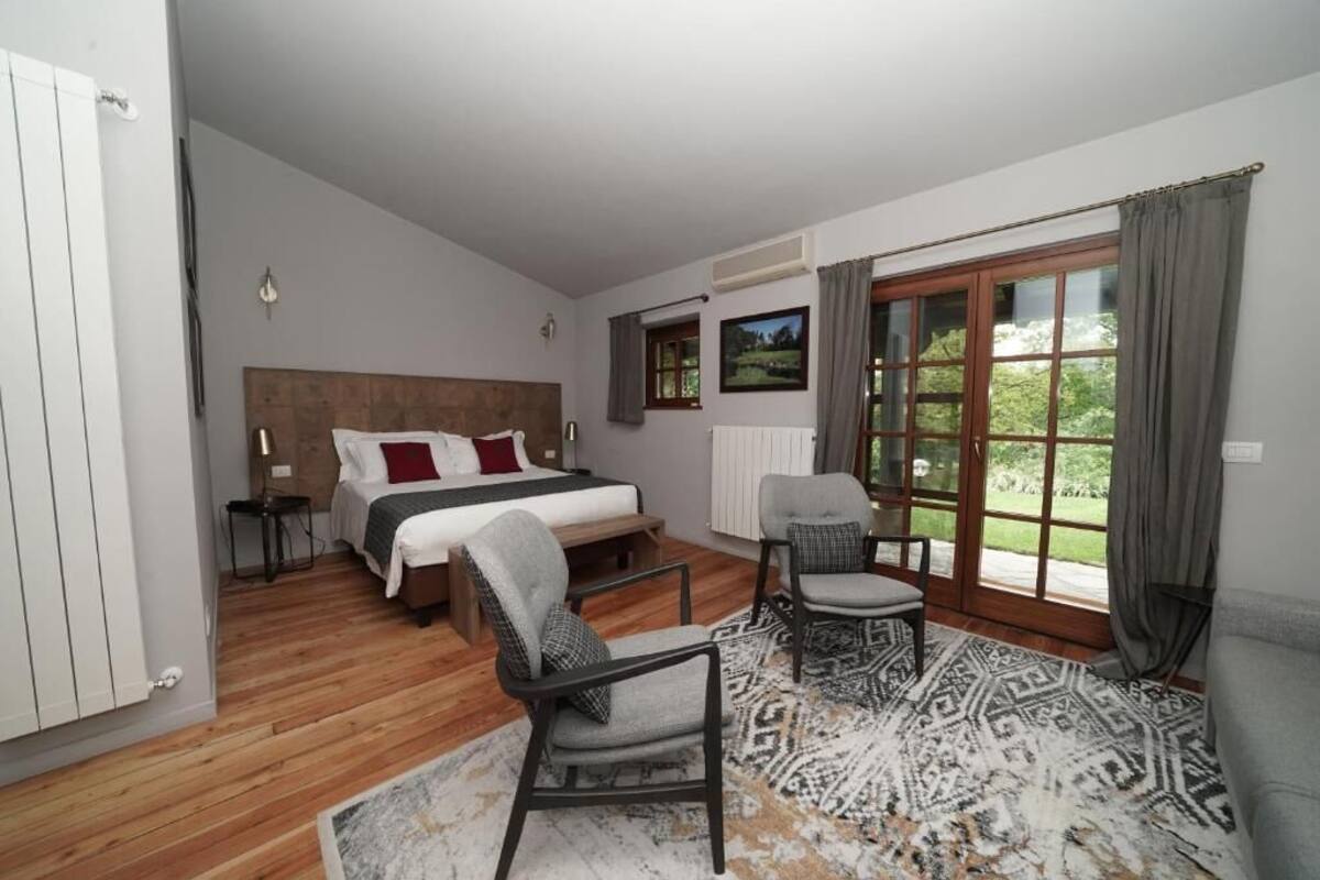 Quarto com cama, duas cadeiras, tapete estampado, janela e radiador.