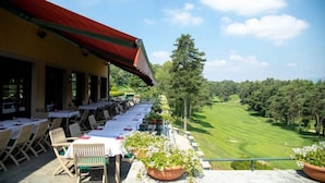 An outdoor dining area with tables and chairs, overlooking a golf course.