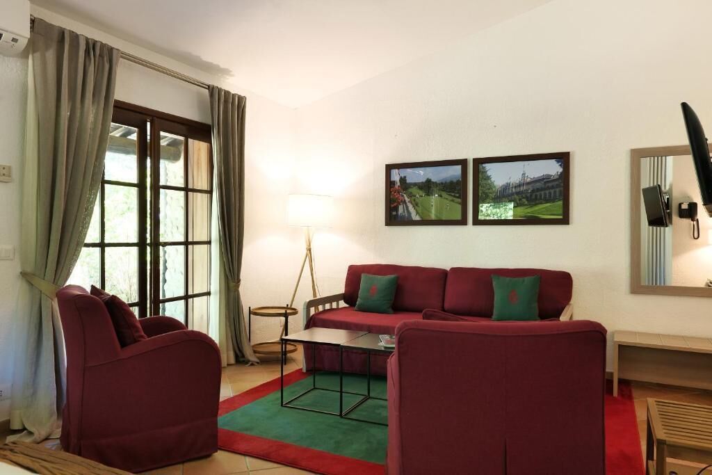 Una sala de estar con un sofá rojo, una alfombra verde, una lámpara y dos cuadros en la pared.