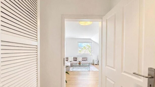 A hallway leading to a living room with a sofa, a coffee table, and a window with a view. - Sea Studio - Modern time-out right on the beach in Scharbeutz (Scharbeutz)