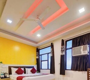 A hotel room with a bed, a ceiling fan, a window with curtains, and an air conditioning unit. - Hotel Airlift at Delhi Airport (New Delhi)