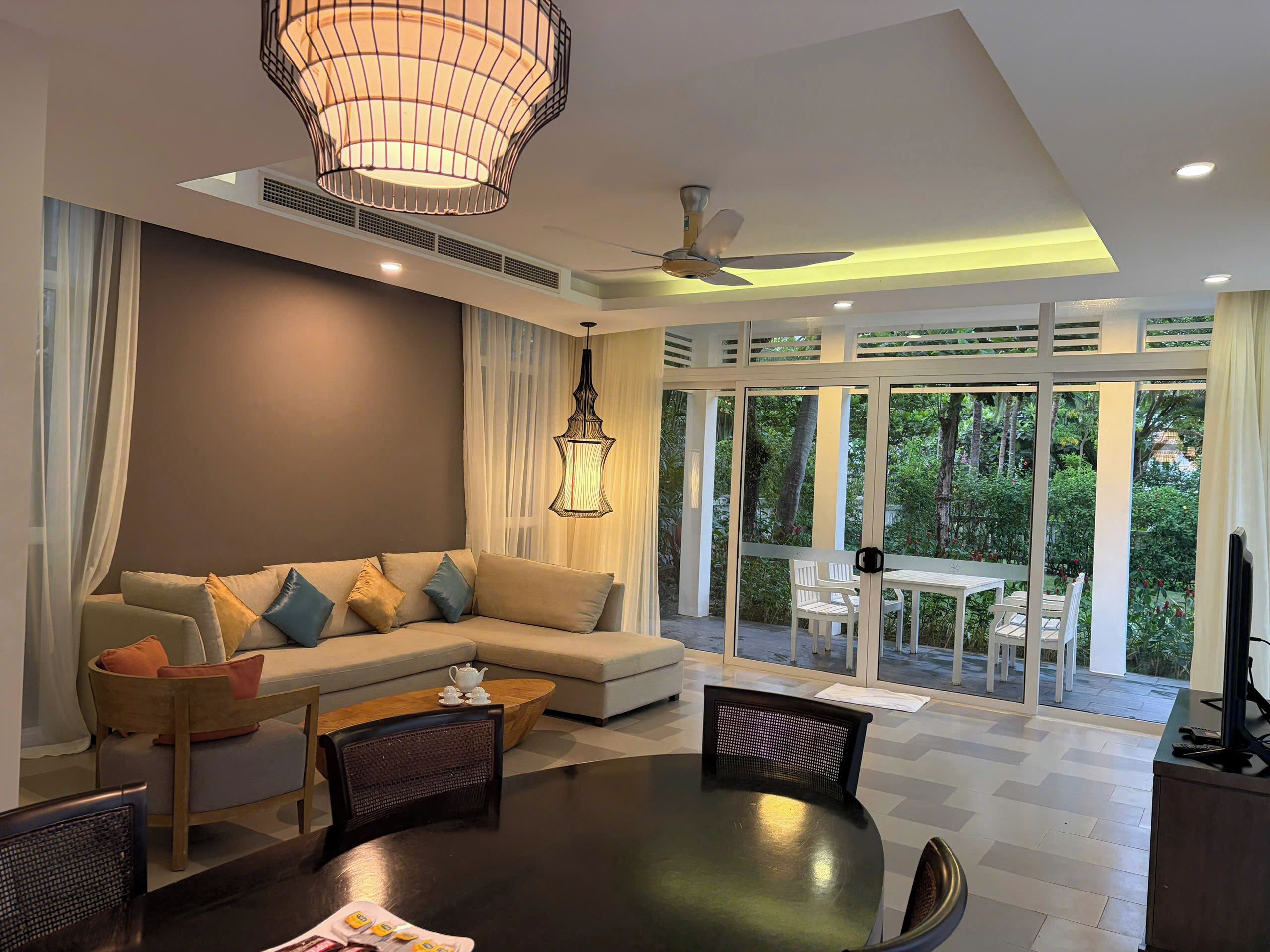 A modern living room with a sectional sofa, dining table, chairs, and a large window offering a view of the outdoors.