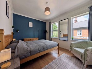 A bedroom with a bed, bedside table, lamp, and a window with a view of a brick building. - Cosy 2bed house in Reading (Reading)