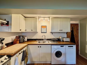 A compact kitchen with white cabinets, a built-in washing machine, a stove, and a sink. - Cosy 2bed house in Reading (Reading)
