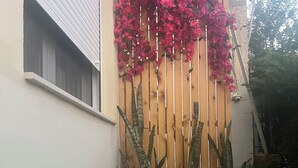 Ein Holzzaun mit rosa Blüten und hohen, grünen Pflanzen.