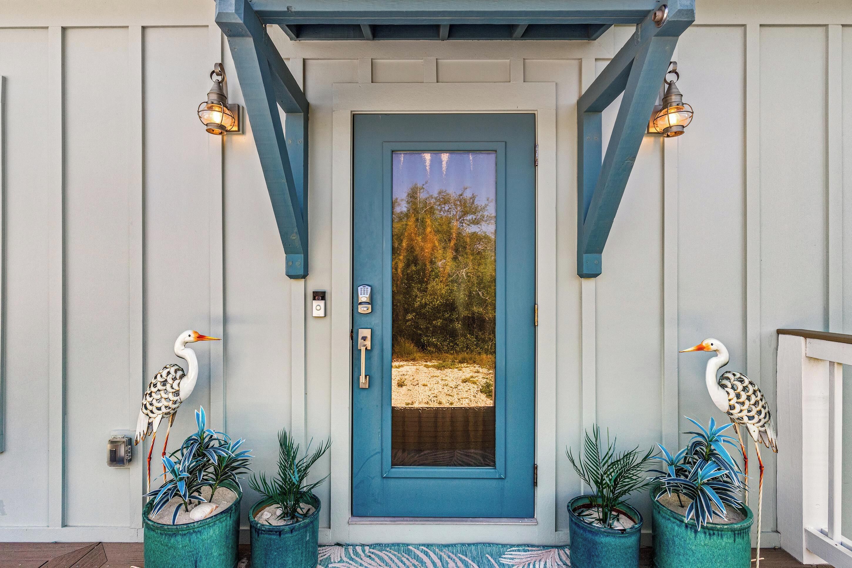 A front door with a blue frame, two decorative birds, and potted plants.