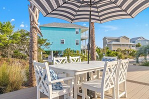 Eine Terrasse mit Tisch und Stühlen, umgeben von Palmen und einem blauen Gebäude im Hintergrund.