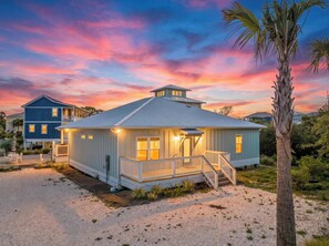 A coastal house with a porch, a staircase, and a palm tree.