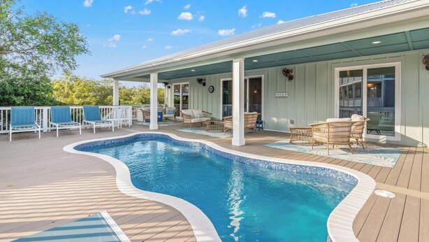 A swimming pool with a wooden deck, lounge chairs, and a covered patio area. - Beach House - Coastal Cabana (Port St. Joe)