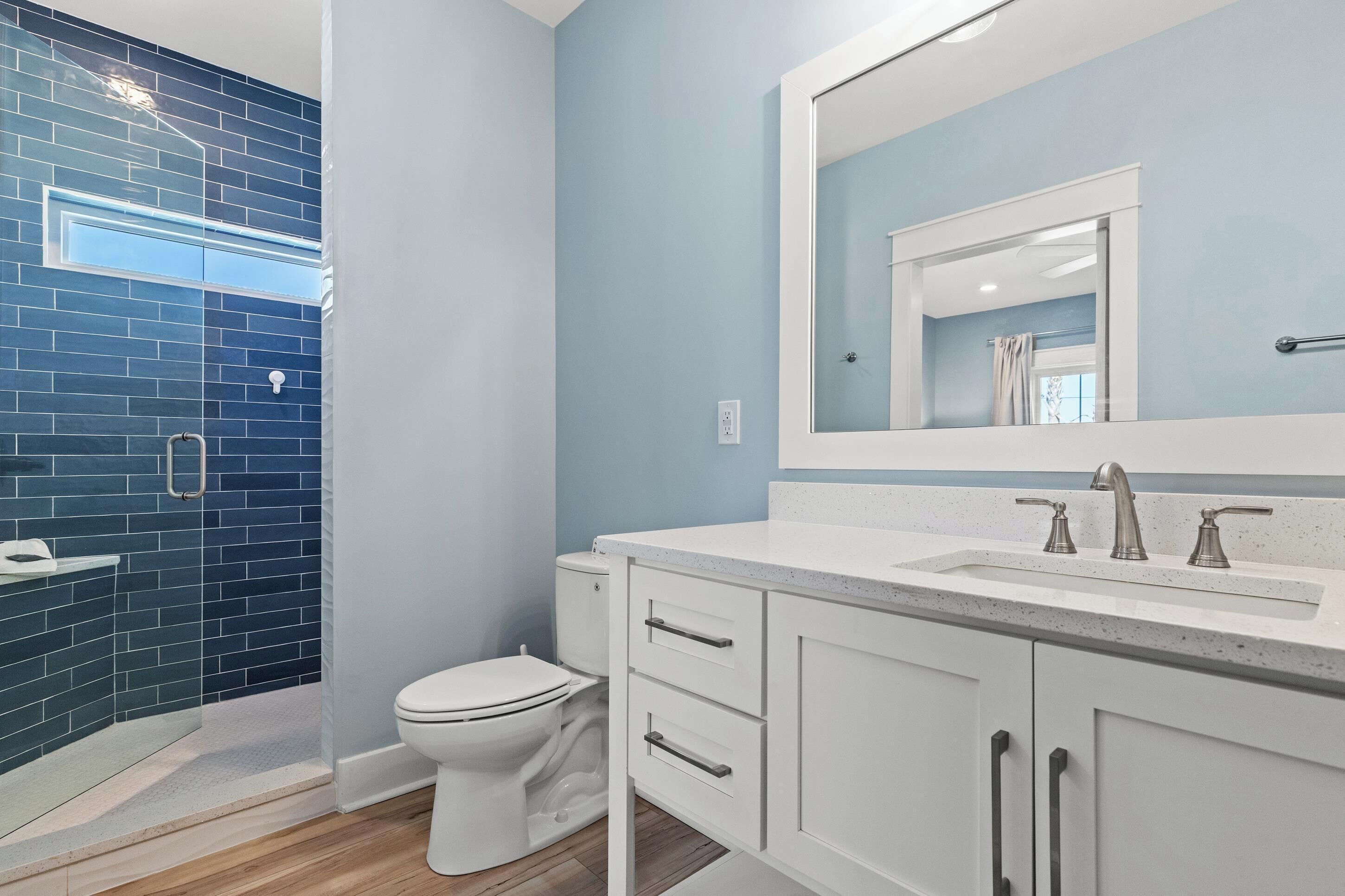 A bathroom with a white toilet, a sink with a large mirror, and blue-tiled walls.