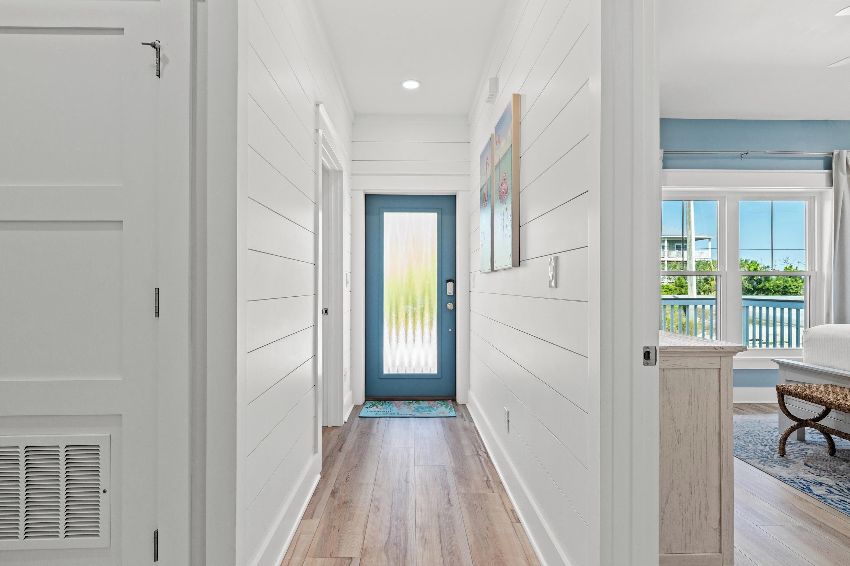 A hallway with a blue door, white walls, and a view of a balcony.