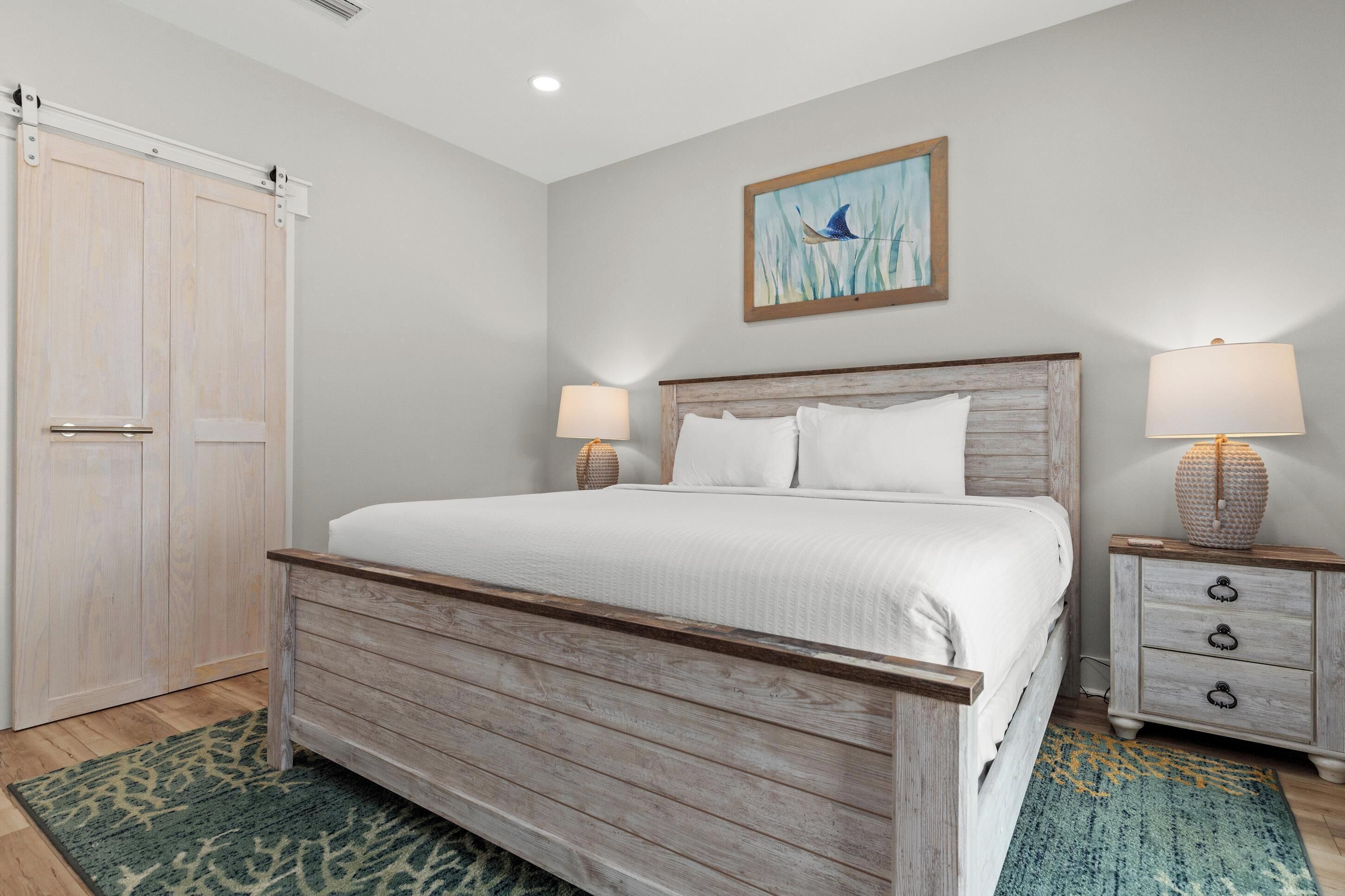 A bedroom with a wooden bed, two bedside tables with lamps, a large window, and a sliding door.