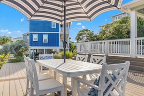 A deck with a table and chairs, a striped umbrella, and a blue house in the background.
