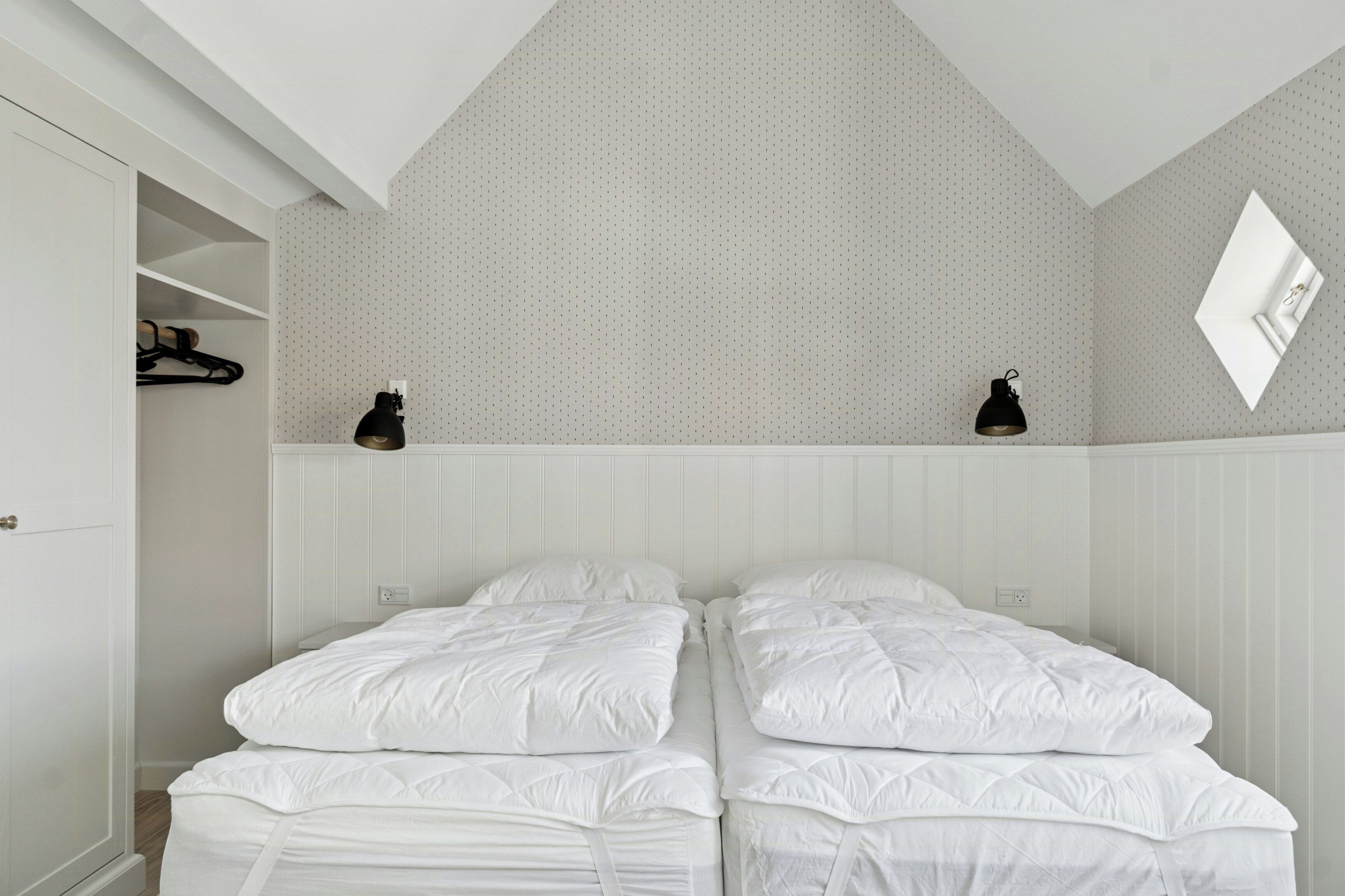 Een slaapkamer met twee bedden, een kledingkast, een spiegel en een plafondlamp.