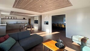 Un espace de vie moderne avec un plafond en bois, un canapé gris, un coin repas et une cuisine.