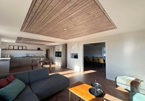 Un espacio habitable moderno con techo de madera, un sofá gris, una zona de comedor y una cocina.