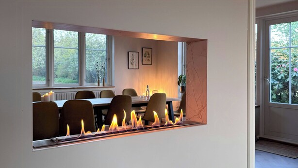 Un intérieur moderne avec une cheminée, un coin repas comprenant des chaises et une table, et de grandes fenêtres.