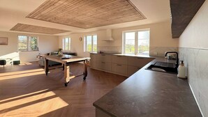 Une cuisine spacieuse avec un plancher en bois, un grand îlot central et une vue sur l’extérieur.