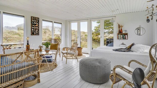 Een ruime kamer met een groot bed, rieten meubels, een rond poef en een boekenkast.