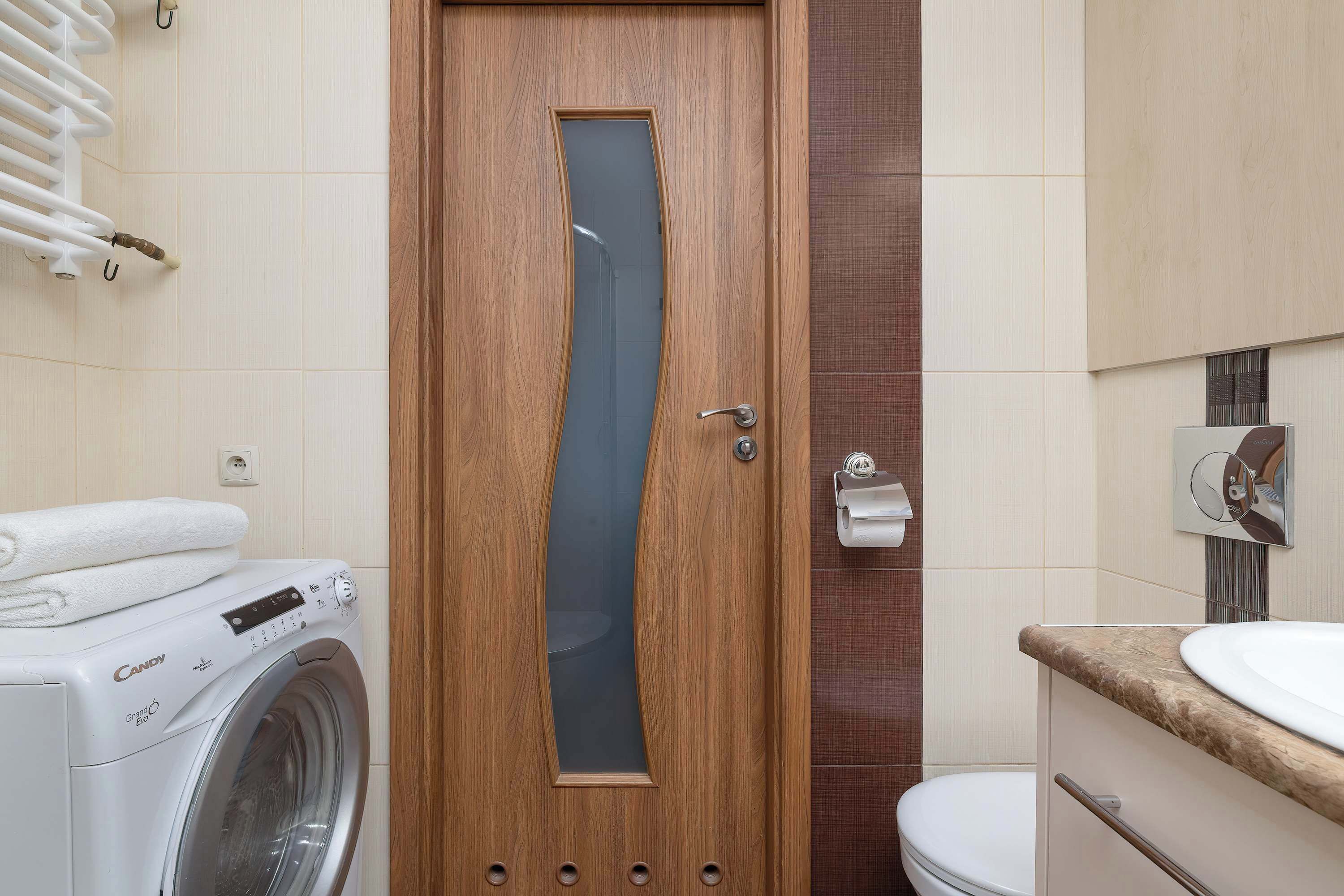 Een badkamer met een houten deur, een wasmachine, een toilet en een wastafel.