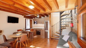 Un grand espace de vie comprenant une table à manger, des chaises, un canapé, une cuisine équipée et un escalier.