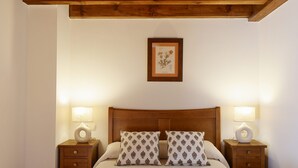 Un lit bien fait, avec deux oreillers, deux tables de chevet avec des lampes, une estampe botanique encadrée au mur et des poutres en bois au-dessus du lit.