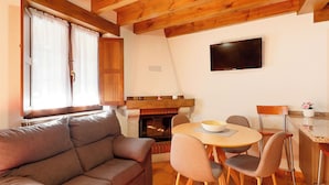 Un salon confortable avec un canapé, une table à manger, des chaises, un téléviseur à écran plat et une cheminée.
