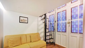Un sofá amarillo, una escalera metálica negra y una puerta blanca con ventanas de tono morado.