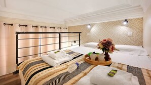 Habitación de hotel con cama, mesita de noche con toallas y bandeja, un jarrón decorativo y pared con estampado.