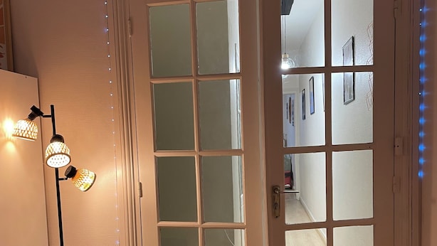 Een kamer met een witte deur, een vloerlamp en led-strips langs het plafond.