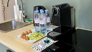 Een kitchenette met een magnetron, koffiezetapparaat, spoelbak en een klein aanrecht met waterflesjes en kruiden.
